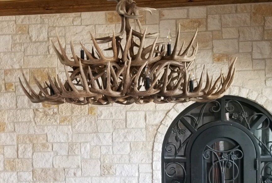 Custom oval whitetail antler dining table chandelier in a stone-walled tasting room.