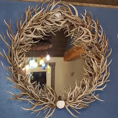 Round mirror framed by natural, handcrafted deer antlers displayed in a dining room setting.