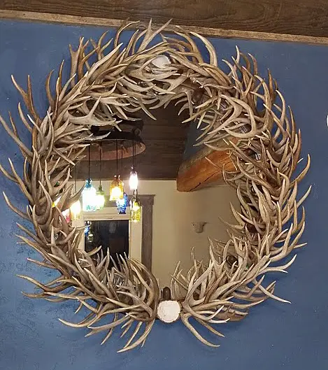 Round mirror framed by natural, handcrafted deer antlers displayed in a dining room setting.