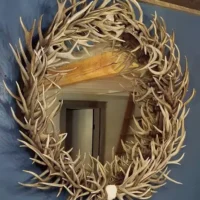 Round wall mirror handcrafted from genuine whitetail antlers with a rustic wooden back