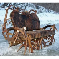 Handcrafted rustic sofa with a frame made from genuine shed deer antlers and premium hair-on-hide upholstery, set in a snowy landscape.