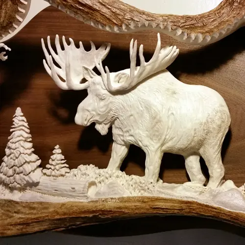 Handcrafted antler carving of a bull moose and pine trees, perfect for rustic lodge gifts.