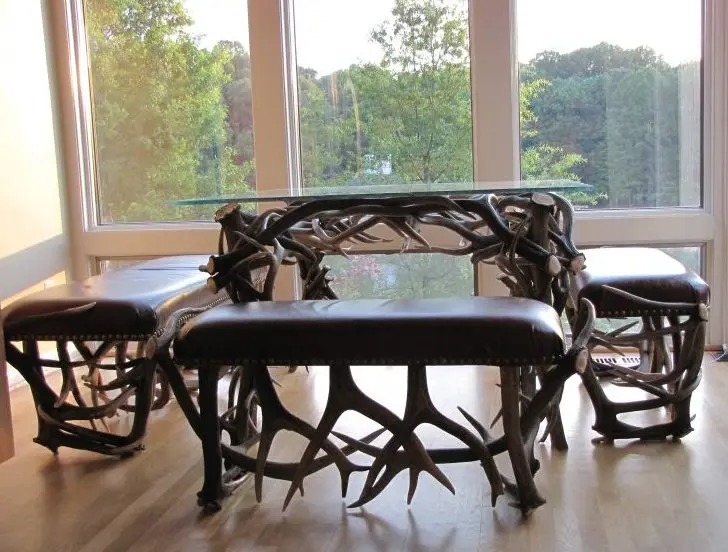 Custom handcrafted antler table and bench set by a large window overlooking a lake.