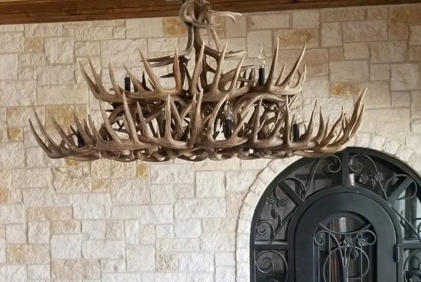 Custom oval whitetail antler dining table chandelier in a stone-walled tasting room.
