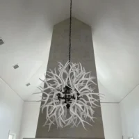 Large modern white deer antler chandelier installed in a high-ceiling dining room
